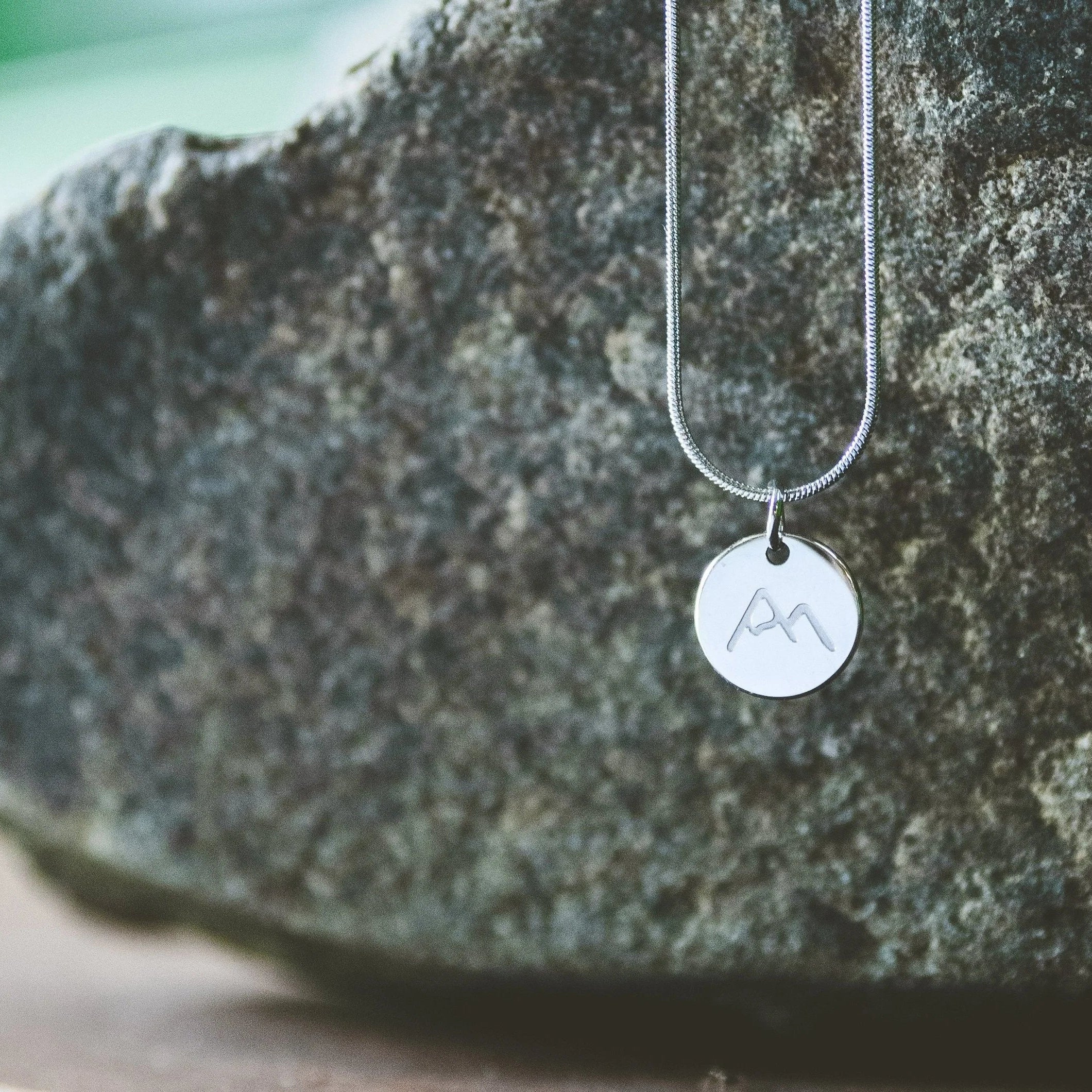 Silver necklace with engraved mountain pendant on a stone surface